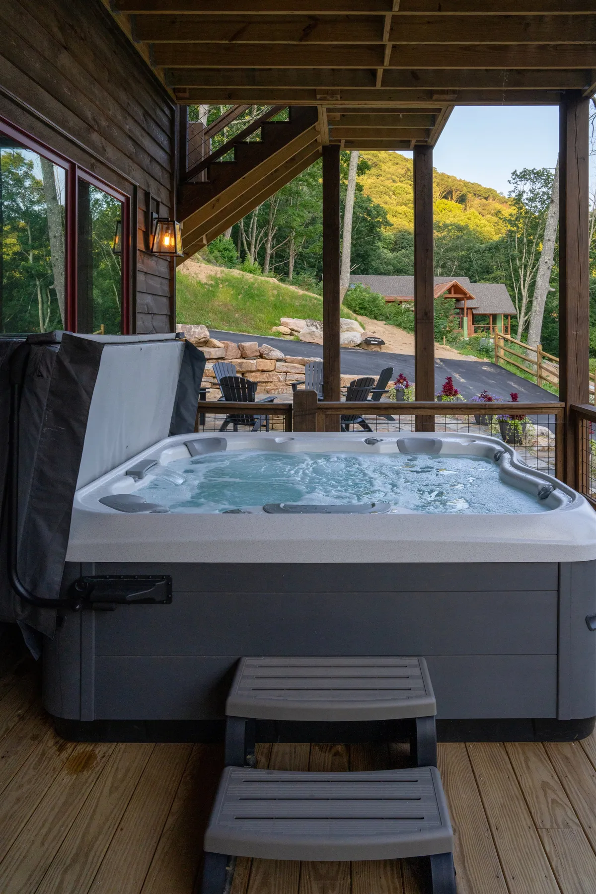 A serene exterior shot showcasing a private hot tub on a wooden deck, surrounded by the natural beauty of the mountains. The scene is tranquil, with hints of sunset light illuminating the area, evoking relaxation and the promise of stargazing nights.