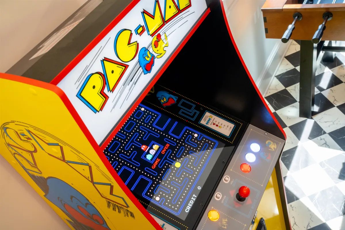 A cozy interior with a Pac-Man arcade machine and a foosball table side by side, inviting guests to gather, play, and share laughter. The decor is casual and welcoming, reinforcing the sense of shared fun and nostalgia.