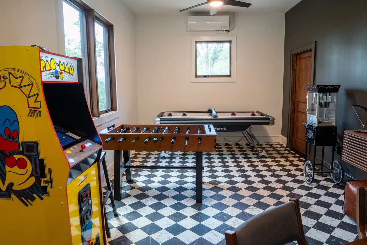 A vibrant game room featuring a Pac-Man arcade machine, foosball table, air hockey table, and a popcorn machine. The room is filled with playful energy and is purpose-built for a variety of games and activities enjoyed by all ages.