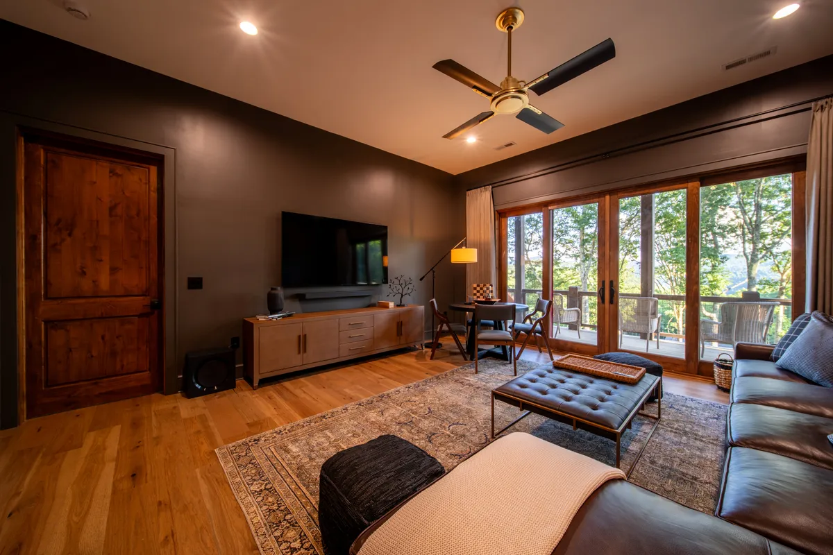 A cozy and stylish interior living area featuring large windows with mountain views, comfortable seating, a modern entertainment unit, and warm lighting—suggesting a perfect space for group gatherings, movie nights, or fireside evenings.