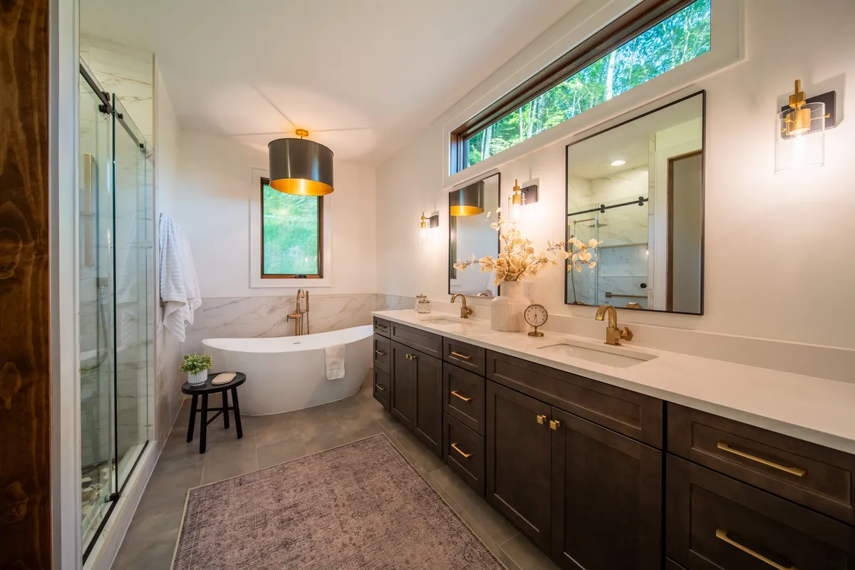 A spa-like bathroom with a freestanding soaking tub, dual vanities with mirrors, and large windows letting in natural light. The clean design and luxurious fixtures evoke a sense of indulgence and relaxation.